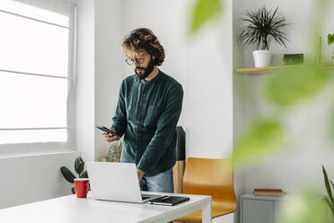 Freelancer using mobile phone at desk in office - XLGF03150