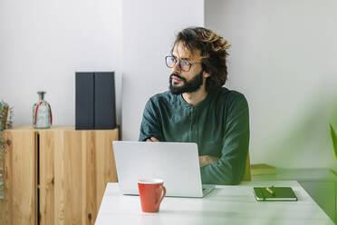 Thoughtful freelancer sitting with laptop at desk - XLGF03164