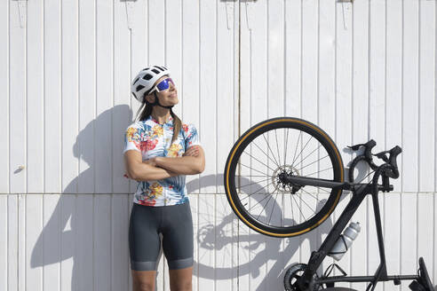 Radfahrer mit Sonnenbrille und Helm, der an einem sonnigen Tag am Fahrrad steht - JCMF02323