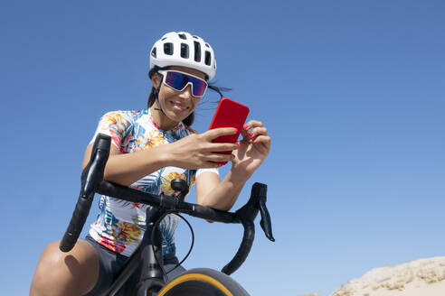 Glücklicher Radfahrer, der auf dem Fahrrad sitzend ein Smartphone benutzt - JCMF02338