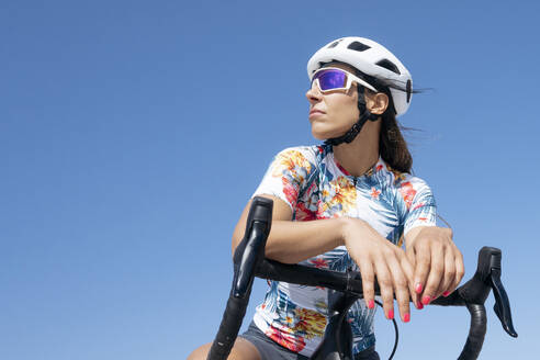 Radfahrer mit Helm auf dem Fahrrad sitzend unter blauem Himmel - JCMF02339