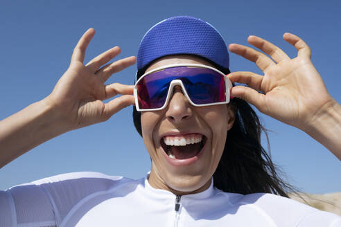 Fröhlicher Radfahrer mit Sonnenbrille und Mütze unter dem Himmel stehend - JCMF02347