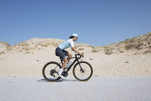 Älterer Radfahrer fährt mit dem Fahrrad auf einer Straße durch Sanddünen - JCMF02348