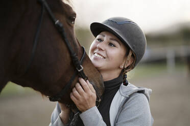 Glückliche Frau mit Helm, die ein Pferd umarmt - NJAF00097