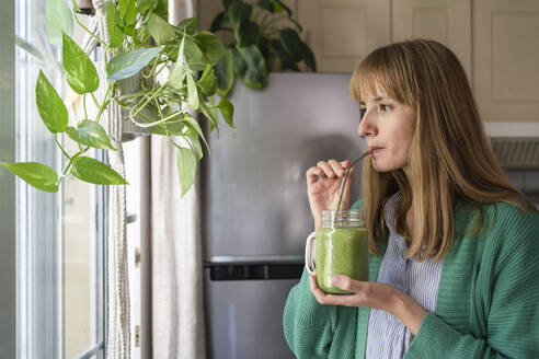 Frau trinkt grünen Smoothie zu Hause - SVKF00939