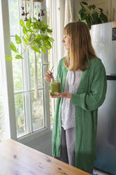 Blonde Frau mit grünem Smoothie schaut aus dem Fenster - SVKF00940