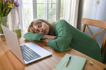 Tired freelancer sleeping on table in kitchen at home - SVKF00946