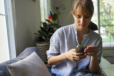 Frau benutzt Smartphone auf Sofa zu Hause - SVKF00983