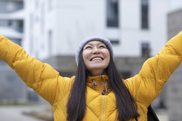 Happy woman wearing knit hat standing with arms raised - SGF02945