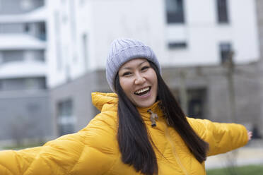 Cheerful woman wearing knit hat standing with arms outstretched - SGF02946