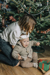 Schwester spielt mit kleinem Bruder vor dem Weihnachtsbaum - VSNF00244