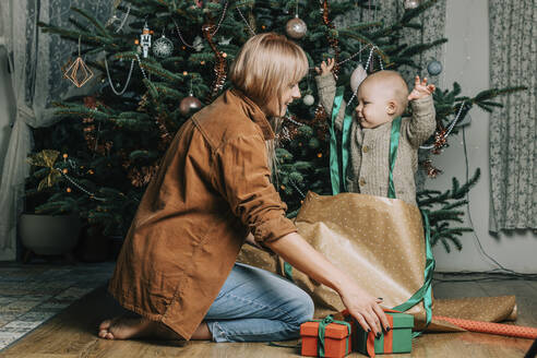 Glückliche Mutter mit ihrem Sohn, der zu Hause am Weihnachtsbaum spielt - VSNF00249