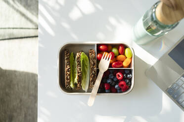 Rye bread, berries and salad with disposable fork in lunch box on table - SVKF00986