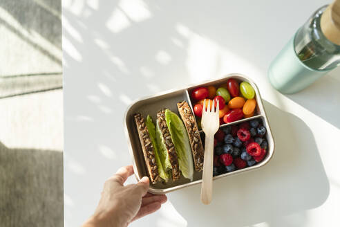 Hand einer Frau, die eine Lunchbox mit gesundem Essen auf dem Tisch hält - SVKF00988