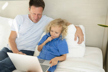 Mann sitzt bei seiner Tochter und benutzt einen Laptop auf dem Bett zu Hause - SVKF00991