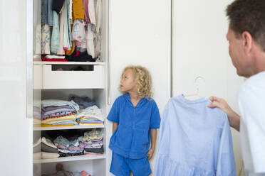 Father holding dress looking at daughter leaning on closet - SVKF01007