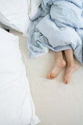 Beine eines Mädchens unter der Bettdecke auf dem Bett zu Hause - SVKF01029