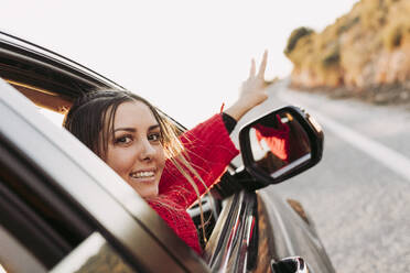 Woman in car looking at camera pointing at road - LJF02380