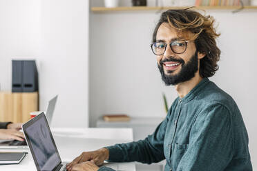 Happy freelancer with laptop at desk in office - XLGF03179