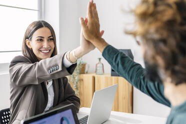 Smiling businesswoman giving high-five to colleague at workplace - XLGF03180