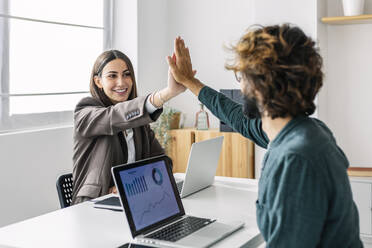 Lächelnde junge Geschäftsfrau, die einem Kollegen am Schreibtisch ein High Five gibt - XLGF03181