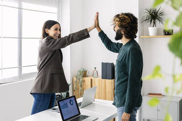 Happy businesswoman giving high-five to colleague in office - XLGF03182