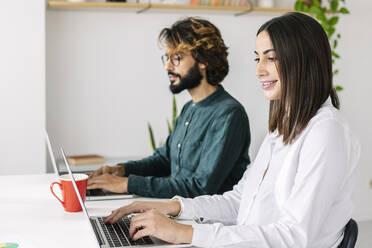 Smiling freelancer with colleague working at desk in office - XLGF03191