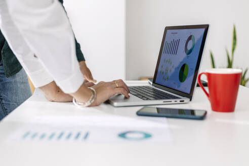 Hands of businesswoman using laptop in front of colleague at desk - XLGF03197