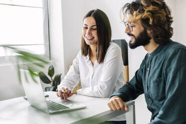 Happy businesswoman using laptop by colleague at desk - XLGF03207