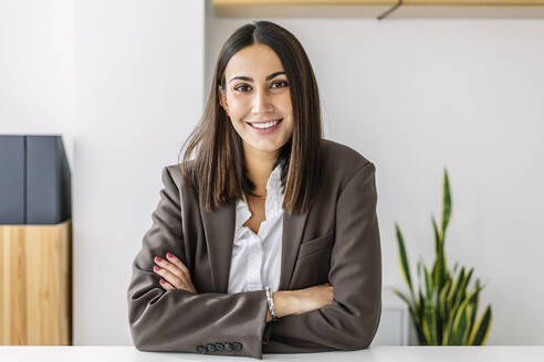 Smiling young businesswoman with arms crossed at workplace - XLGF03218