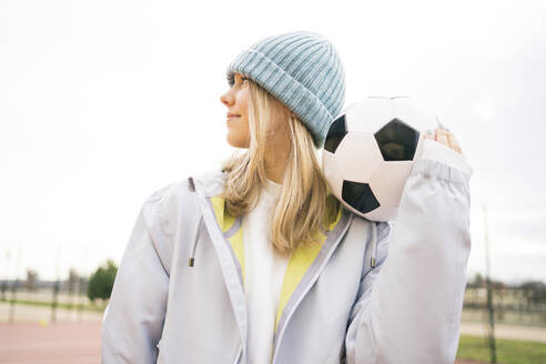 Teenager-Mädchen mit Strickmütze, stehend mit Fußball - MDOF00438