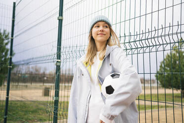 Nachdenkliches Mädchen mit Strickmütze, stehend mit Fußball - MDOF00445