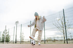 Glückliches Mädchen im Teenageralter spielt mit Fußball auf dem Spielplatz - MDOF00446