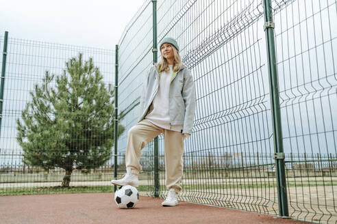 Teenager-Mädchen steht mit Fußball am Zaun auf dem Spielplatz - MDOF00460