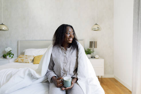 Glückliche junge Frau mit Kaffeetasse auf dem Bett zu Hause - TYF00513