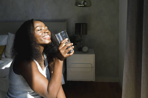 Happy woman holding drinking glass enjoying at home - TYF00517