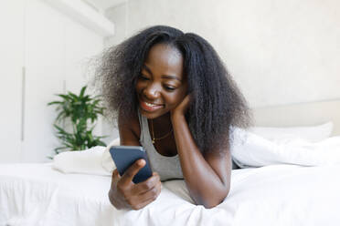 Happy woman lying on bed using mobile phone at home - TYF00520