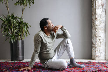 Thoughtful man sitting on carpet at home - EYAF02442