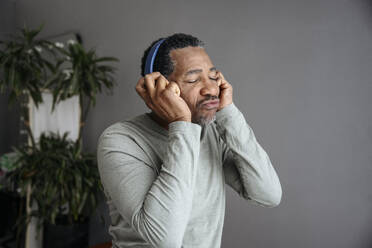 Älterer Mann, der über drahtlose Kopfhörer vor einer grauen Wand Musik hört - EYAF02451