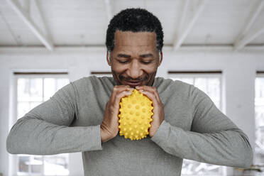 Happy man squeezing yellow stress ball at home - EYAF02454