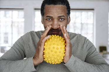 Mature man squeezing yellow stress ball at home - EYAF02455