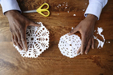 Hands of man holding paper snowflakes on table - EYAF02467