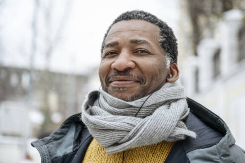 Smiling mature man wearing warm clothing listening to music through in-ear headphones - EYAF02483