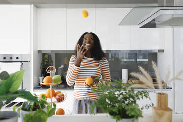 Happy woman juggling oranges in kitchen - TYF00524