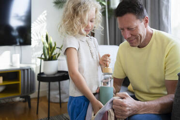 Smiling father with daughter packing water bottle in backpack - SVKF01032