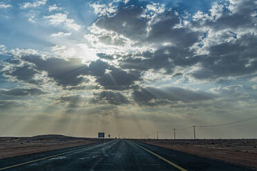 Saudi-Arabien, Al-Ula, Untergehende Sonne durchdringt Wolken über leerer Autobahn - RUNF04879