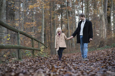 Glückliches Mädchen hält die Hand des Vaters und geht im Herbstwald spazieren - NJAF00108