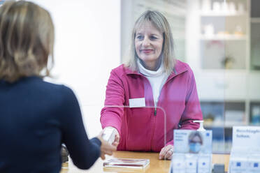 Lächelnde Apothekerin, die einem Kunden Medikamente gibt - NJAF00124