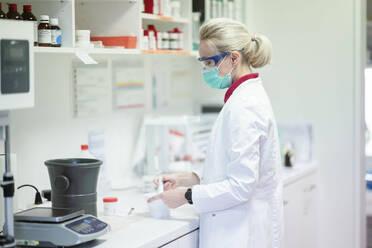Scientist wearing protective face mask making medicine in laboratory - NJAF00126
