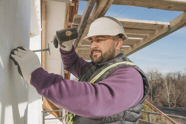 Bauarbeiter schlägt mit dem Hammer auf die Wand, um Polystyrolschaum zu installieren - OSF01265